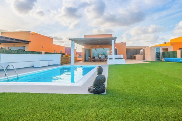 A modern outdoor pool area with a Buddha statue, a covered seating area, and a clear sky.