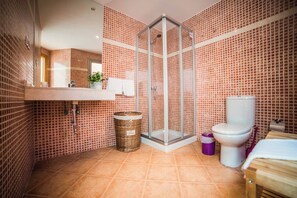 A bathroom with a glass-enclosed shower, a white toilet, a sink with a mirror, and a tiled floor.
