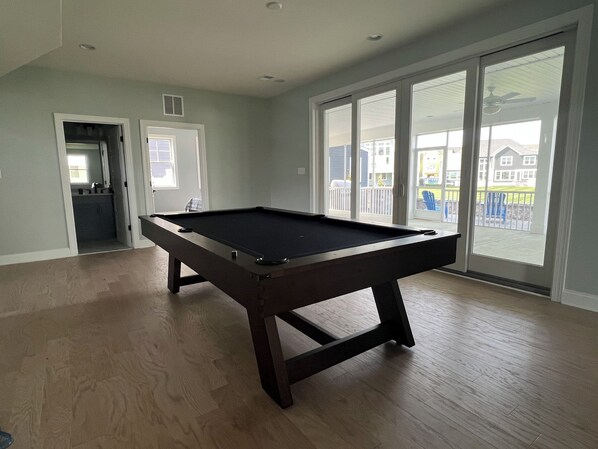 A pool table in a room with large windows and a view of a residential area. - Beautiful Family Vacation Home. The Peninsula - Exclusive 5 Star Gated Community (Millsboro)