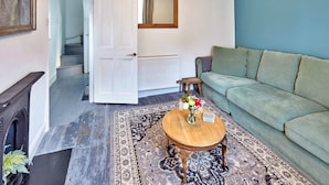A living room with a green sofa, a wooden coffee table with a vase of flowers, a patterned rug, and a staircase leading to another room. - Albion Cottage (Whitby)