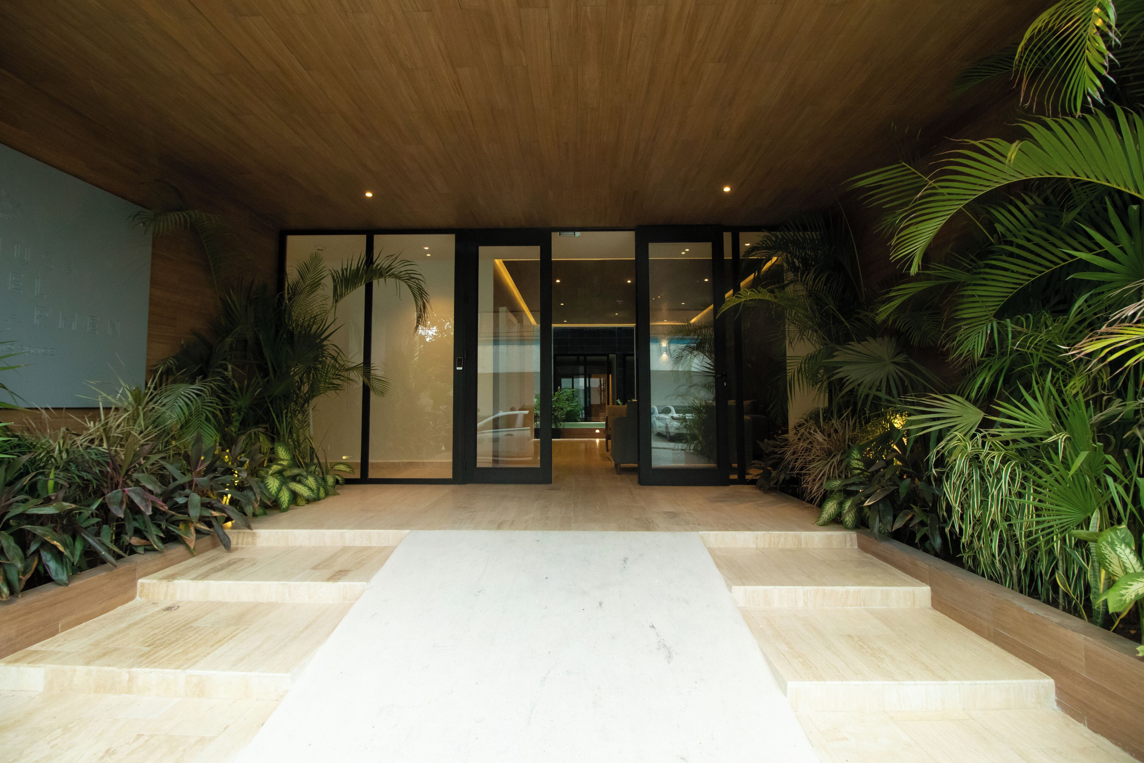 Une entrée moderne, avec un plafond en bois, des portes en verre et un chemin central en marbre.