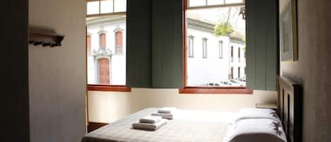 A hotel room with a bed, a nightstand, and a window with a view of a building.