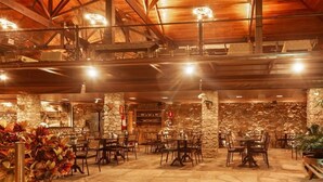 A spacious indoor dining area with stone walls and wooden beams, featuring multiple tables and chairs. - Hotel Quadrado  (Santa Barbara)