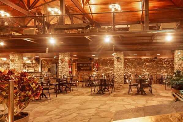Un amplio comedor interior con paredes de piedra y vigas de madera, con varias mesas y sillas.