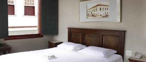 A hotel room with a large bed, a wooden headboard, a framed picture on the wall, and a window with curtains.