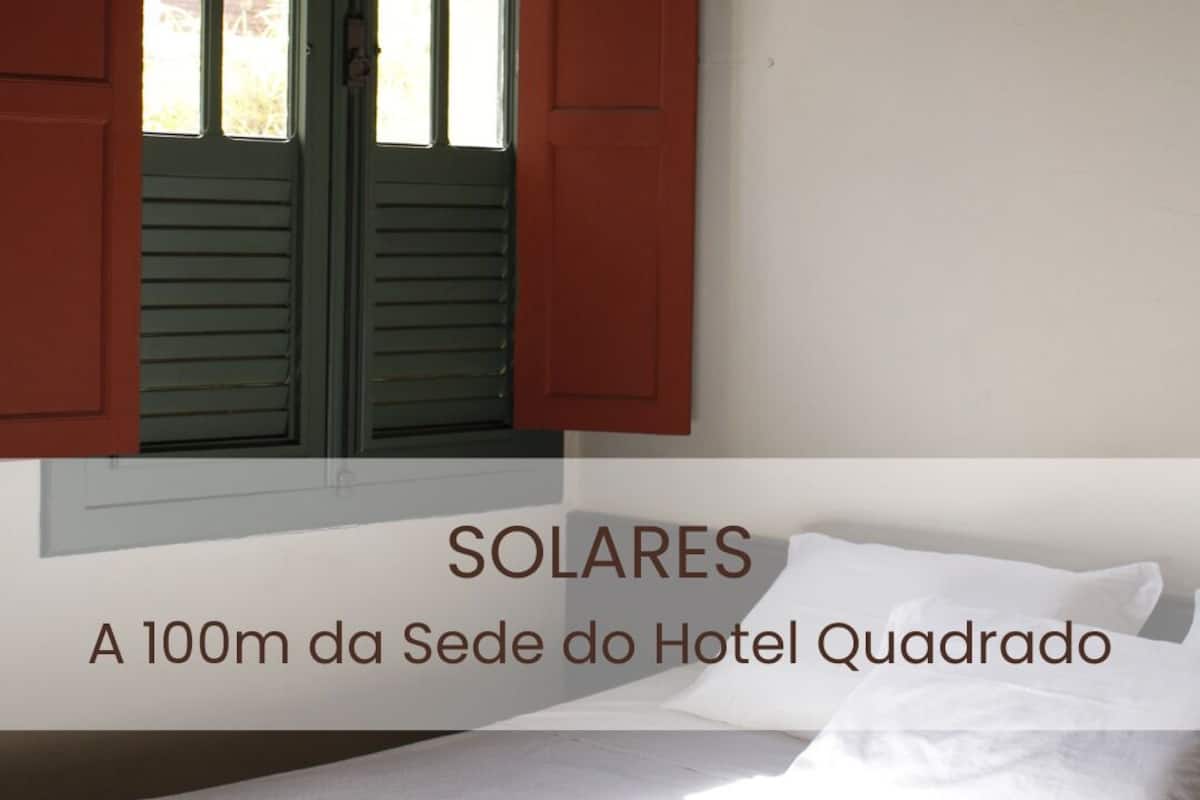A hotel room with a bed, white linens, and a window with shutters.