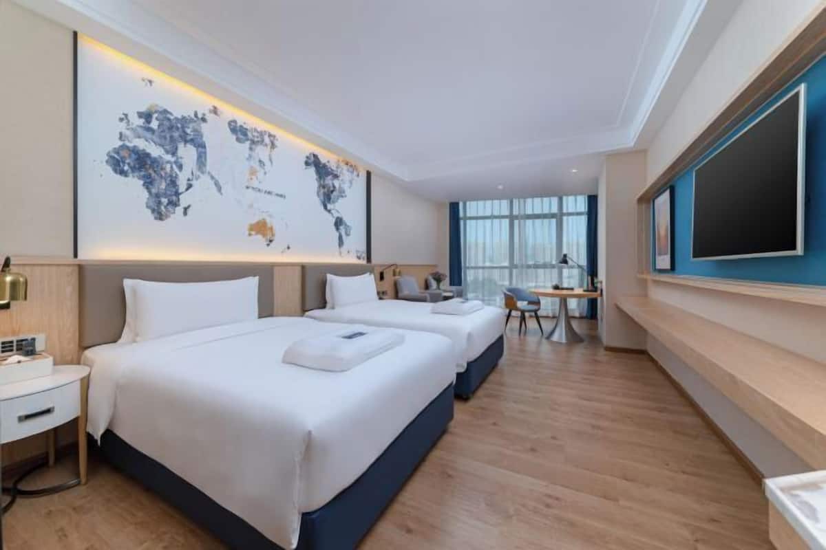 A hotel room with two beds, a desk, a chair, a map on the wall, and a TV.