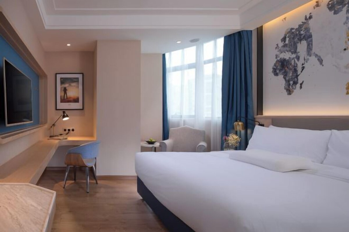 Hotelkamer met een bed, een bureau, een stoel, een televisie en een groot abstract schilderij aan de muur.
