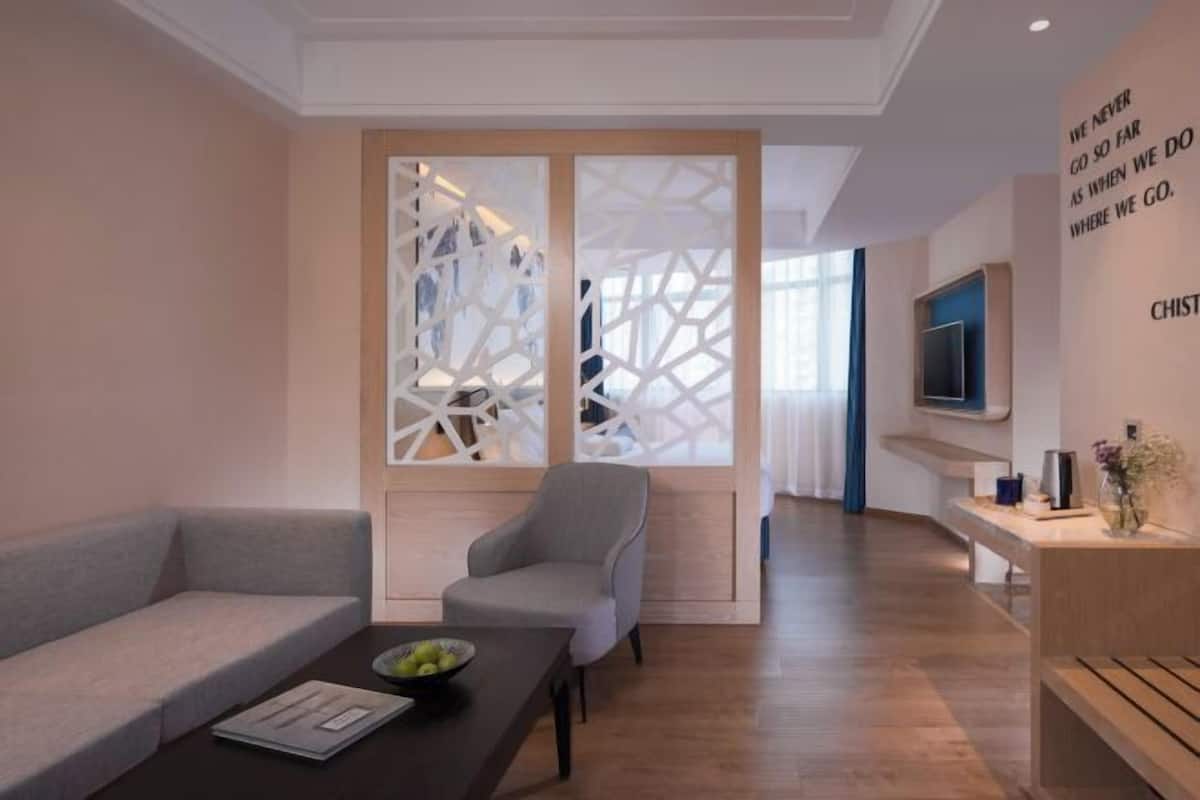 Ein modernes Hotelzimmer mit Sofa, Sessel, Holz-Couchtisch und einem dekorativen Raumteiler.