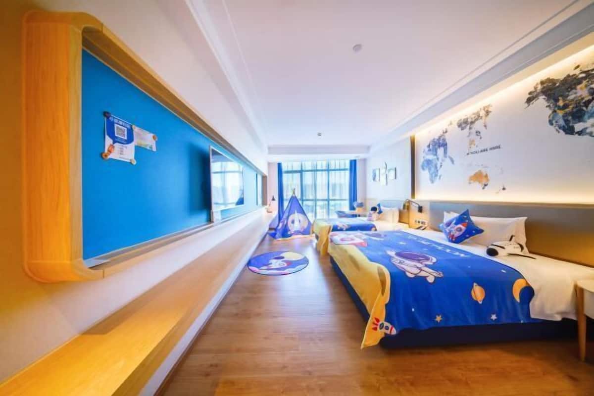 A hotel room with two beds, a large window, a world map on the wall, and a blue and yellow bedspread.