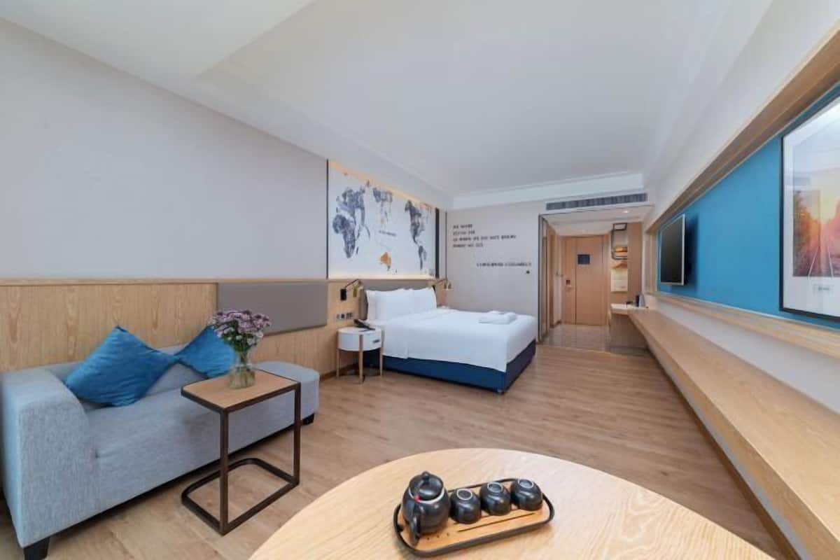A hotel room with a bed, a sofa, a small table with a tray of tea cups, a TV, and a map on the wall.