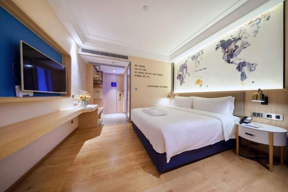 Een hotelkamer met een bed, nachtkastje, televisie en een wereldkaart aan de muur.