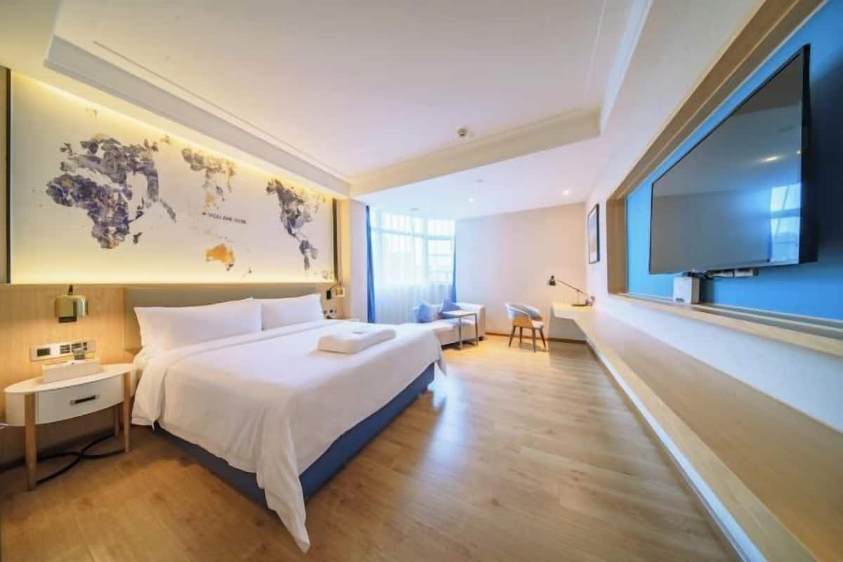 Ein modernes Hotelzimmer mit einem großen Bett, einem Schreibtisch, einem Sessel, einem Flachbildfernseher und einer Weltkarte an der Wand.