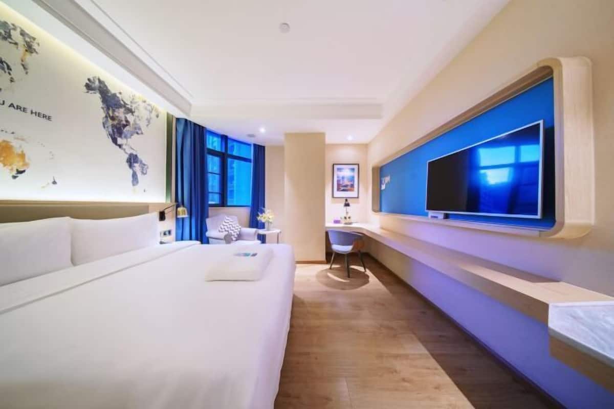 Ein Hotelzimmer mit einem großen Bett, einem Schreibtisch mit Stuhl, einem Flachbildfernseher und einer Weltkarte an der Wand.
