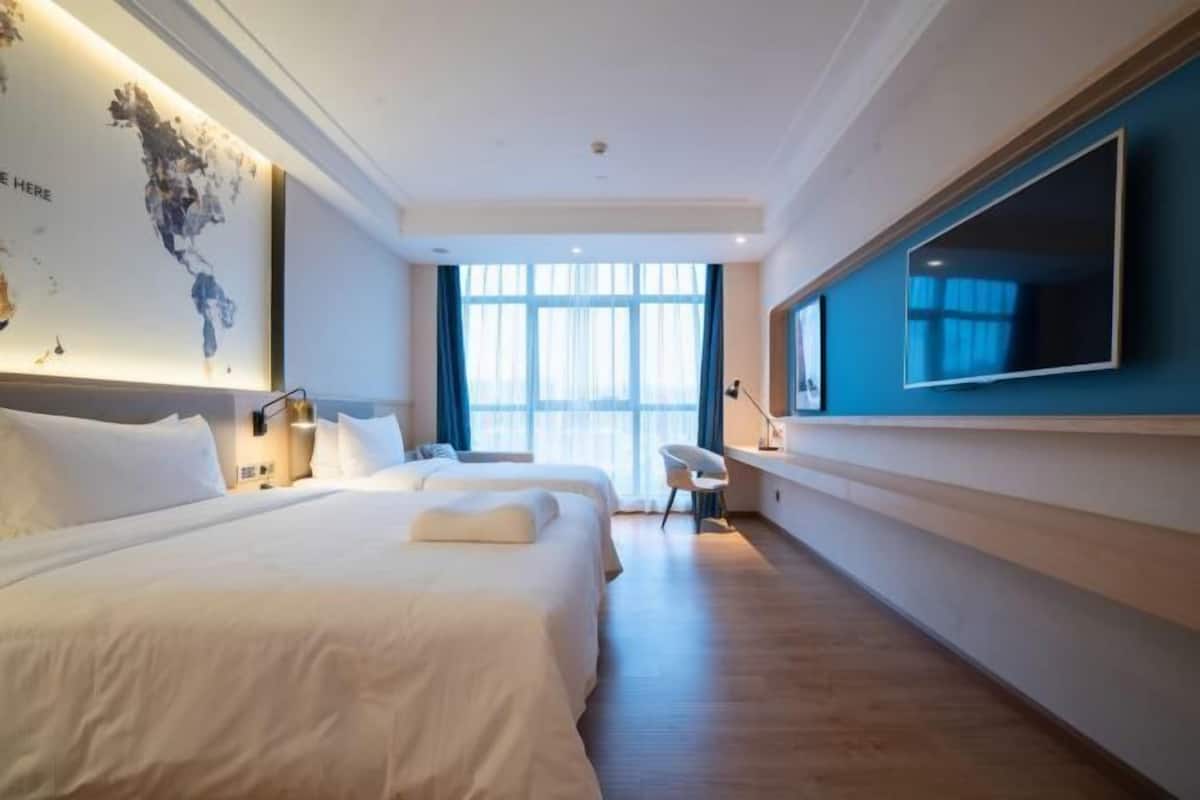 Ein Hotelzimmer mit zwei Betten, einem Schreibtisch, einem Stuhl, einem großen Fernseher und einer Weltkarte an der Wand.