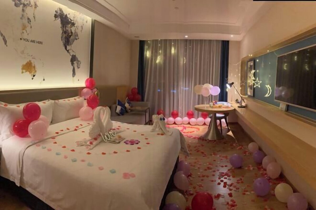 A hotel room with a bed, a desk, a chair, a world map on the wall, and a view of the night sky.
