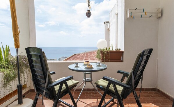 Un patio con dos sillas, una mesa, una lámpara colgante y vista al mar.