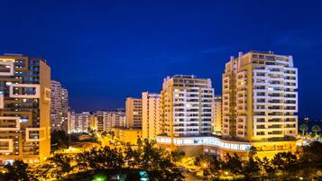 A nighttime view of a residential area with high-rise buildings, a well-lit parking area, and trees.
