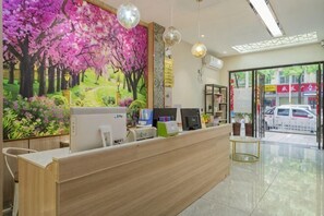 Una recepción con un computador, un teléfono y una planta. Hay un cuadro de un árbol rosado en la pared.
