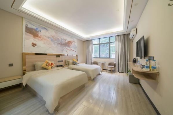 Quarto de hotel com duas camas, um quadro abstrato grande na parede, uma mesinha com cadeiras e uma TV também na parede.