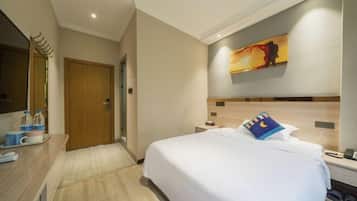 A hotel room with a bed, a desk with a chair, a mirror, a painting on the wall, and a wooden door.