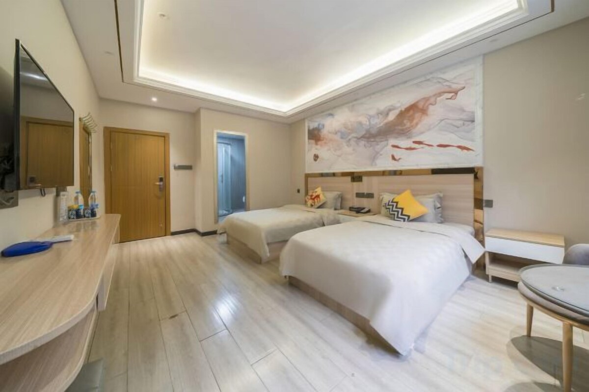 Une chambre d’hôtel avec deux lits, un bureau, une chaise, une télévision et une porte de salle de bain.