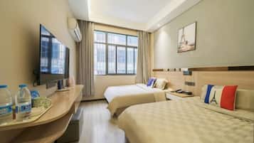 A hotel room with two beds, a desk with a flat-screen TV, a window with curtains, and a painting of the Eiffel Tower.