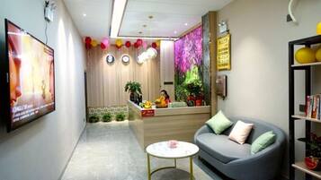 A reception area with a sofa, a small table, a TV, and a reception desk.