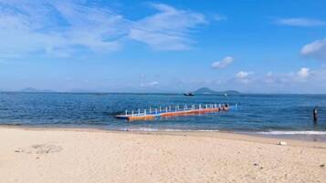 A beach with a clear sky, calm sea, and a wooden walkway extending into the water.