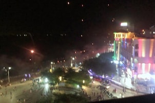 Vista nocturna de una plaza con gente y edificios iluminados.