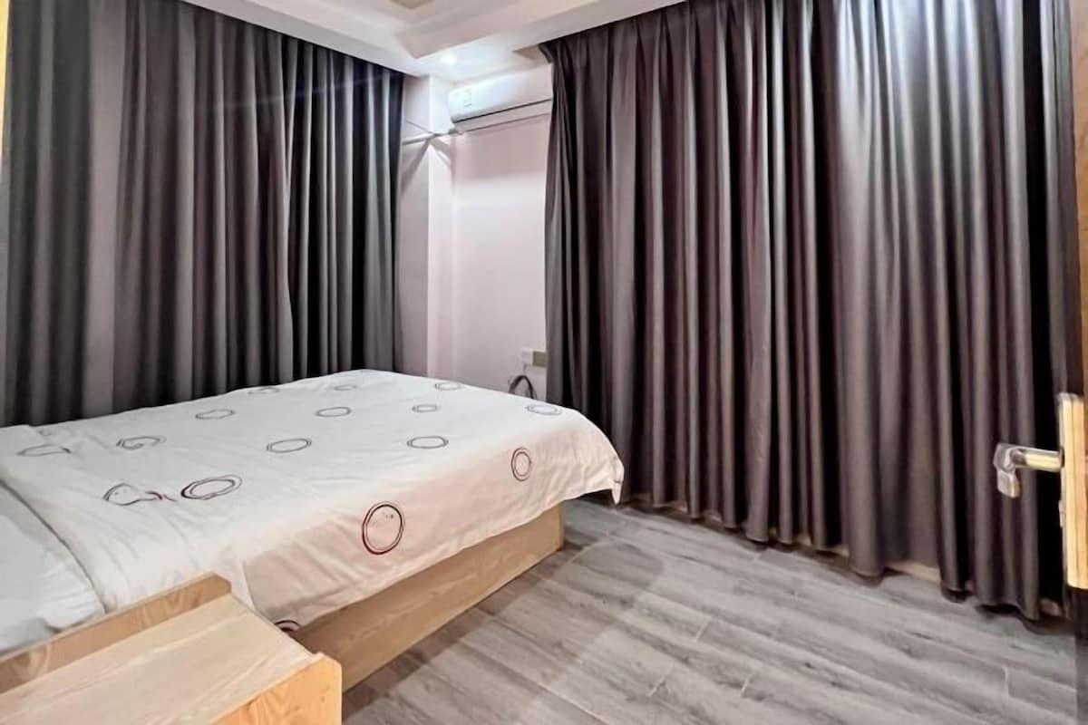 Une chambre à coucher avec un lit, des rideaux, un plancher en bois et une porte.