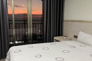 Une chambre d’hôtel avec un grand lit, une table de chevet et une vue sur le coucher de soleil au-dessus d’une ville.