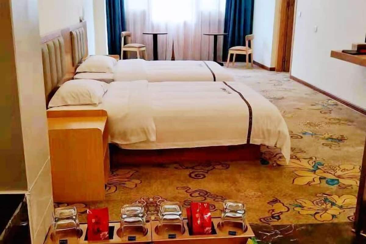 A hotel room with two beds, a wooden headboard, a small table, and a decorative carpet.