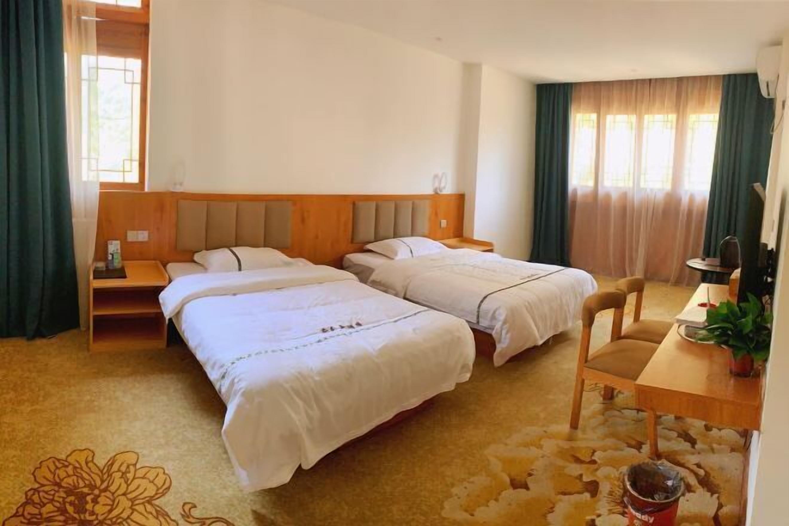 A hotel room with two beds, a wooden headboard, a desk with a chair, and a potted plant.