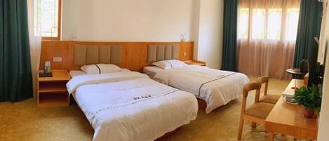 A hotel room with two beds, a wooden headboard, a desk with a chair, and a potted plant.