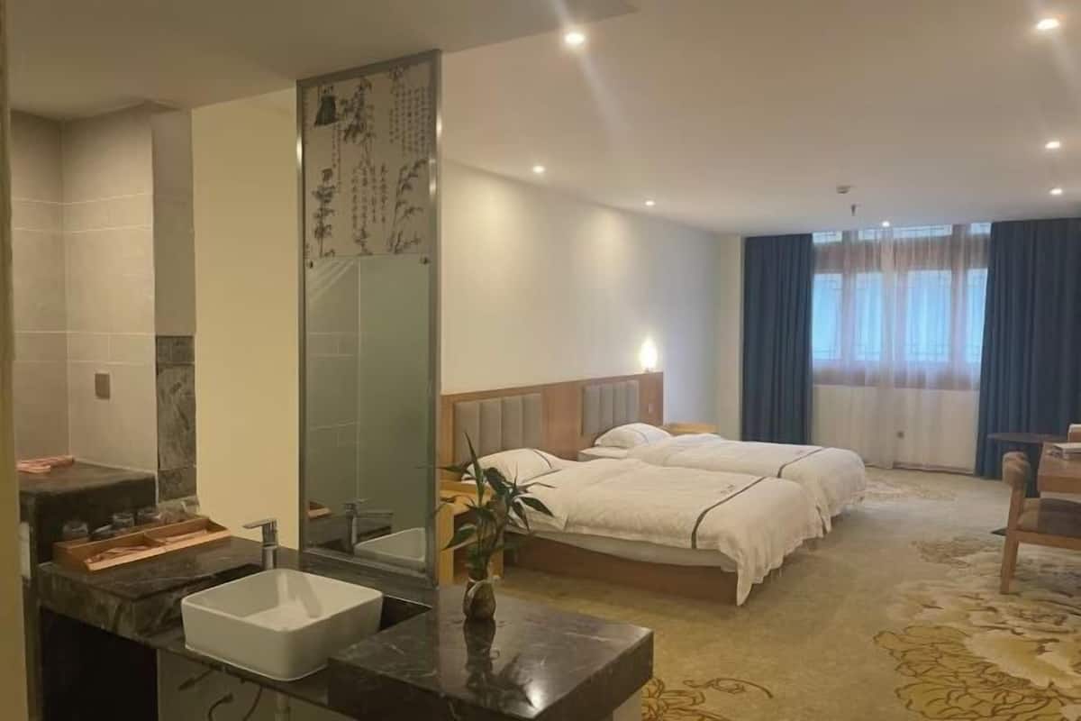 A hotel room with a large bed, a bedside table, a mirror, a sink, and a window with curtains.