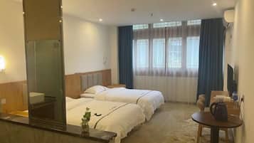 Ett hotellrum med två sängar, ett litet bord, en stol, ett skrivbord, en spegel och ett fönster med gardiner.