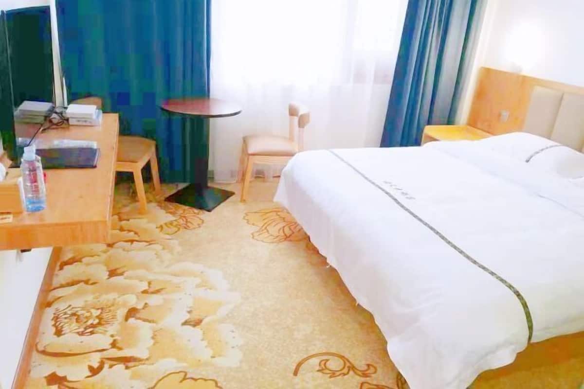 A hotel room with a bed, a desk with a chair, a small table, and a window with curtains.