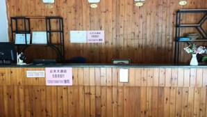 Un mostrador de recepción de madera con certificados y señalizaciones, una silla negra y una pequeña mesa con un florero.