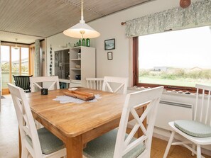 A dining area with a wooden table, white chairs, a hanging light fixture, and a view through a window.