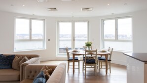 Een ruime woonkamer met een eettafel, twee banken en grote ramen met uitzicht over de stad.