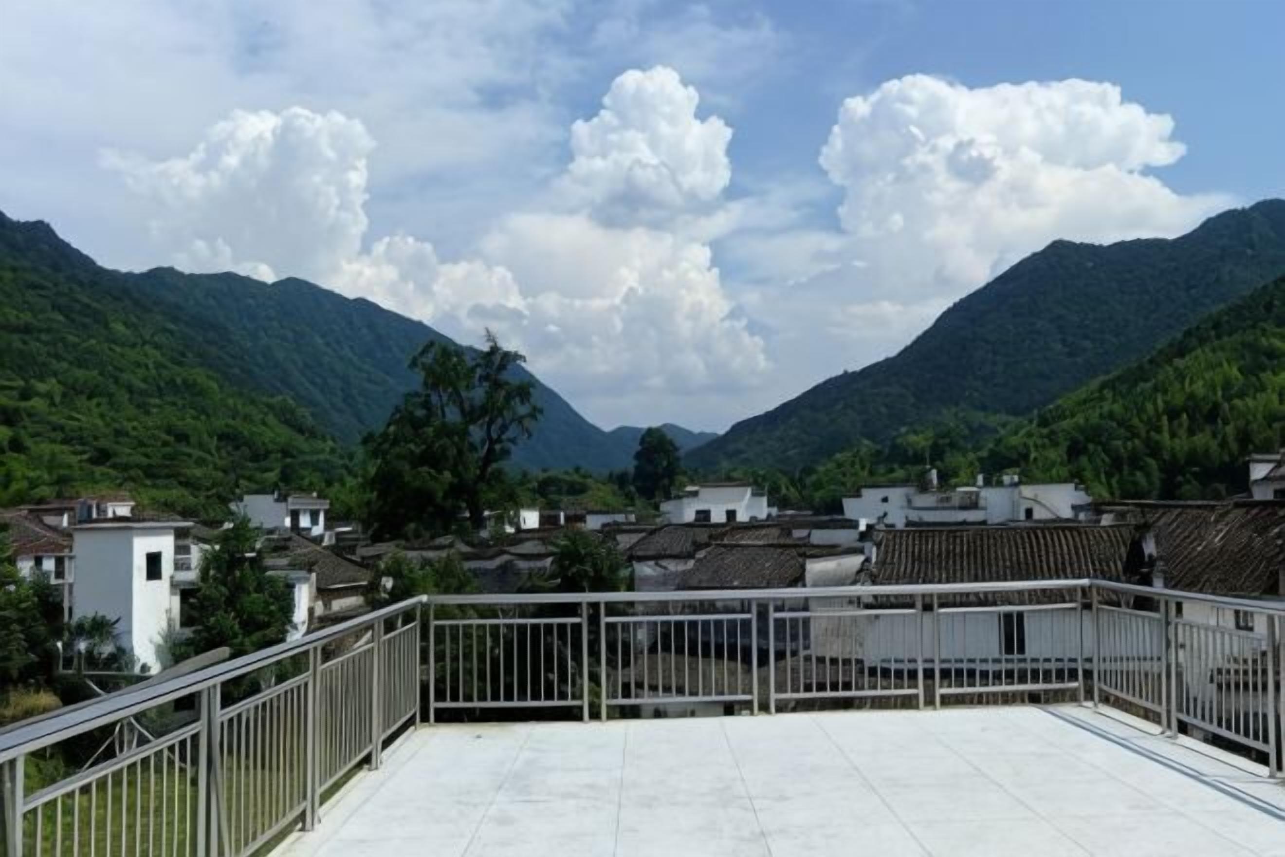 Una terraza en la azotea con barandilla de metal, con vistas a un valle con edificios tradicionales y colinas verdes.