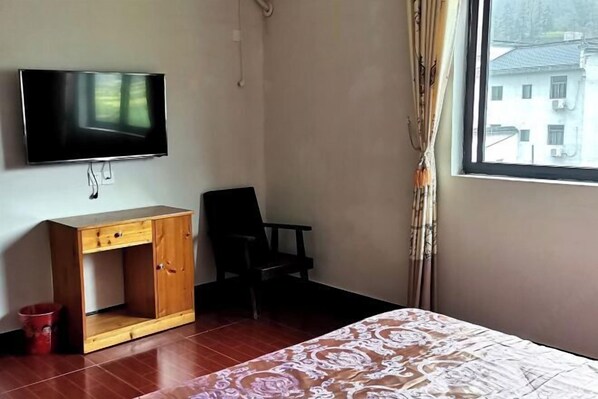 A room with a bed, a wooden desk, a chair, a television, and a window with curtains. - Wuyuan Youyicun Inn (Wuyuan)