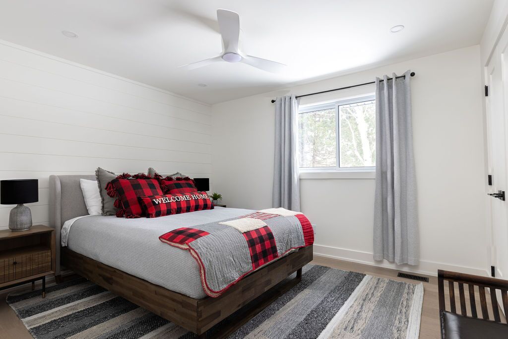 A bedroom with a bed, a nightstand, a ceiling fan, a window with curtains, and a view of trees outside.