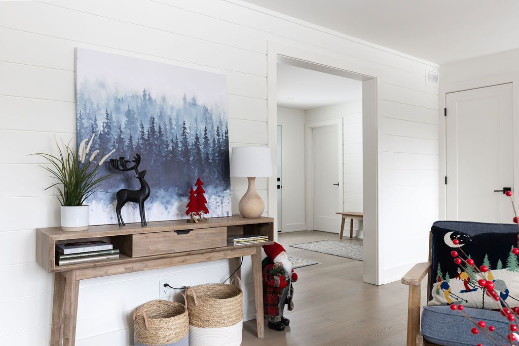 A modern living room with a fireplace, a painting of a forest, and holiday decorations.