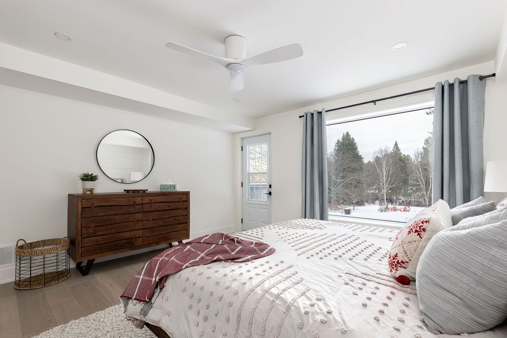 A bedroom with a bed, a dresser, a mirror, and a window with a view of trees.