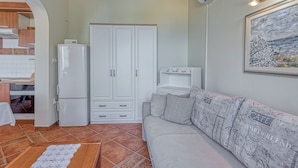Um espaço compacto com cozinha americana, um guarda-roupa branco, um sofá cinza com almofadas estampadas e um quadro na parede.