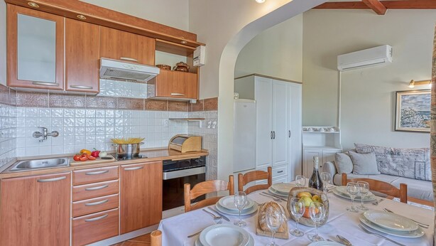 Cozinha com armários de madeira, painel de azulejos brancos e área de refeições com mesa posta para quatro pessoas.