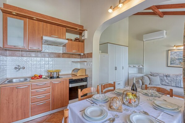 A kitchen with wooden cabinets, a white tiled backsplash, and a dining area with a table set for four. - Valdarke Sea View Apartment /w Balcony (Mali Losinj)