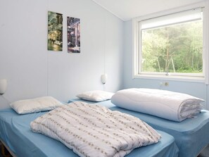 Une chambre avec deux lits, une fenêtre donnant sur la verdure et deux tableaux accrochés au mur.